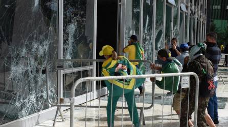 Supporters of Brazilian former President Jair Bolsonaro destroy a window of the the plenary of the Supreme Court in Brasilia on January 8, 2023. - Hundreds of supporters of Brazil's far-right ex-president Jair Bolsonaro broke through police barricades and stormed into Congress, the presidential palace and the Supreme Court Sunday, in a dramatic protest against President Luiz Inacio Lula da Silva's inauguration last week. (Photo by Ton MOLINA / AFP)