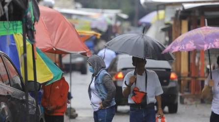 Hondureños caminan por el centro de San Pedro Sula mientras llueve.
