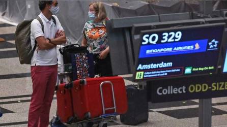 Dos pasajeros con mascarilla llegados de Ámsterdam recogen su equipaje en el aeropuerto Changi de Singapur.
