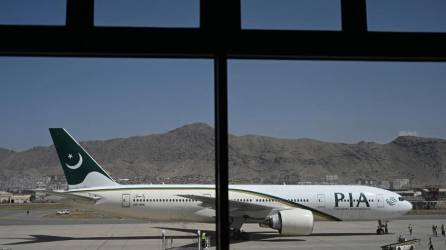 Miembros del personal de tierra están parados en la pista junto a un avión de Pakistan International Airlines.