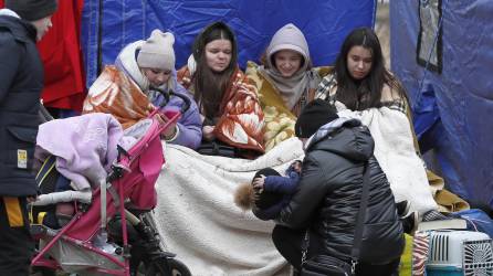 Refugiados ucranianos, cubiertos con mantas, se recuperan frente a una carpa después de pasar el cruce fronterizo rumano-ucraniano en Siret, en el norte de Rumania, el 27 de febrero de 2022.