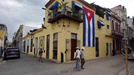 Transeúntes caminan frente a una casa adornada con una bandera cubana hoy, en La Habana.