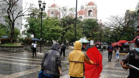 Personas se protegen de la lluvia en el parque central de San Pedro Sula.