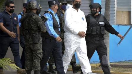 Miembros de la Policía hondureña escoltan al ex alcalde hondureño Arnaldo Urbina Soto, vestido con un traje de bioseguridad, para ser entregado a las autoridades estadounidenses hoy, en la base aérea Soto Cano, en Palmerola (Honduras).