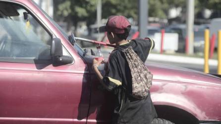 Un niño hondureño limpia el vidrio frontal de un vehículo en una calle de San Pedro Sula.