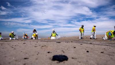Varias personas recogen el alquitrán de la playa después de un derrame de petróleo frente a la costa de Huntington Beach