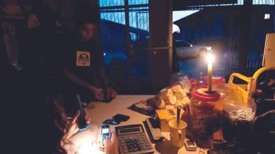 Hondureños a oscuras, alumbrándose con una candela, en un pequeño negocio.