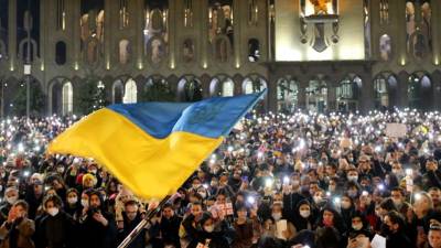 Manifestantes con antorchas encendidas mientras se ondea una bandera ucraniana durante una manifestación en apoyo al país invadido por Rusia.