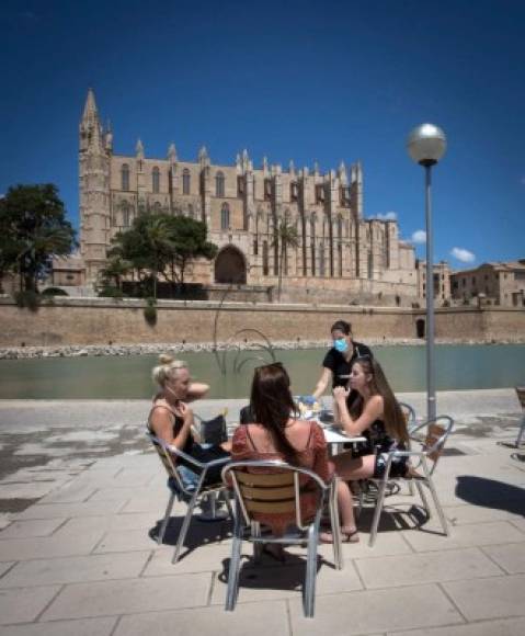 A waitress wearing a face mask serves costumers at a terrace bar near the Cathedral in Palma de Mallorca on May 11, 2020, as Spain moved towards easing its strict lockdown in certain regions. - Spaniards returned to outdoor terraces at cafes and bars as around half of the country moved to the next phase of a gradual exit from one of Europe's strictest lockdowns (Photo by JAIME REINA / AFP)