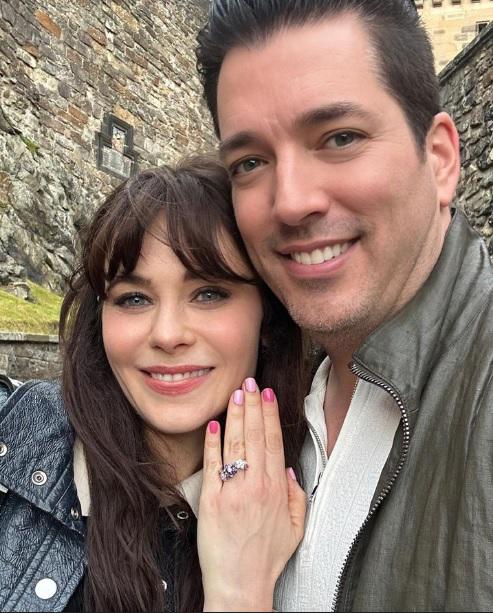 Zooey Deschanel luciendo orgullosa su anillo de compromiso, confeccionado con pequeñas piedras de color rosa, blanco y morado, y de diseño floral.