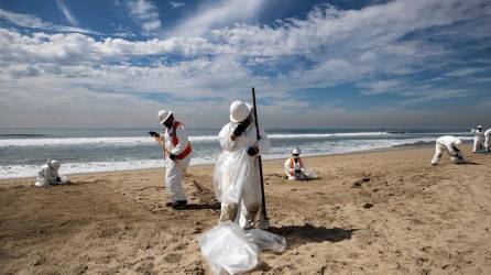 Personal de limpieza recoge el alquitrán de la playa después de un derrame de petróleo frente a la costa de Huntington Beach.