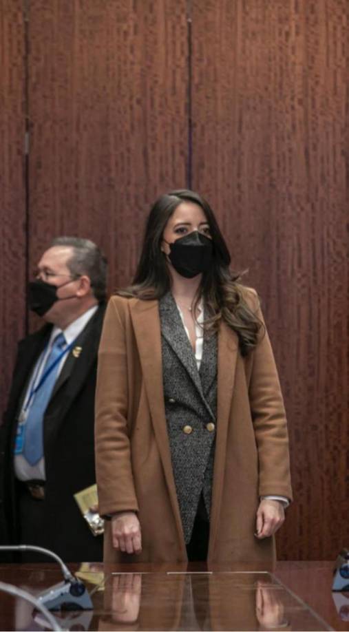 Aquí luce un pantalón formal negro, un blazer gris con textura de punto y un abrigo café. 