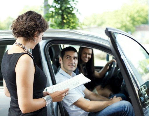 Couple talking to salespersons at car showroom.