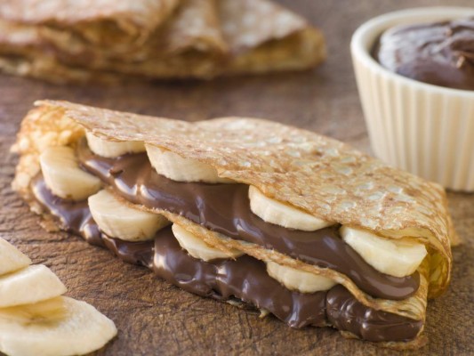 Crepes on chopping board filled with banana and chocolate hazelnut spread