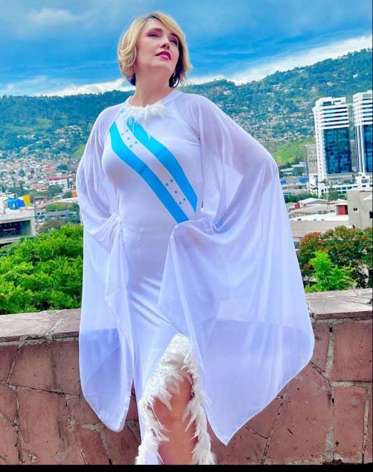Judith Bellino de Canal 11 luce un hermoso vestido blanco con detalles de plumas y la bandera de Honduras estampada en su pecho.