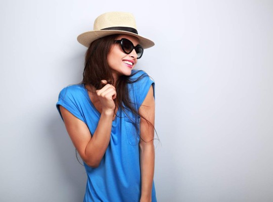 Happy enjoyment young woman in sun glasses and hat posing on blue background