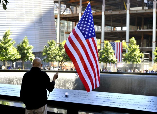 epa03394000 Maicia Rodriguez holds a US flag in a moment of silence at the South Tower pool during observances held on the eleventh anniversary of the attacks on the World Trade Center, at the site in New York, 11 September 2012. EPA/TIMOTHY A. CLARY / POOL