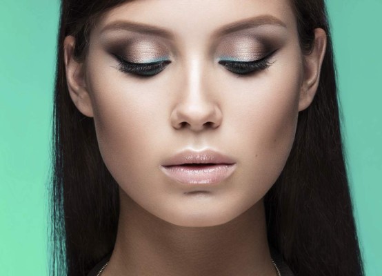 Beautiful woman with evening make-up and long straight hair . Smoky eyes. Fashion photo. Picture taken in the studio on a green background.