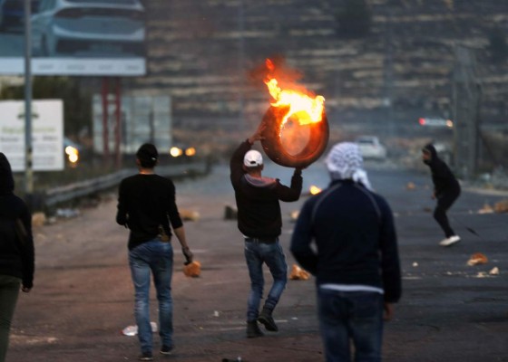A Palestinian protester carries a burning tire during clashes with Israeli forces near an Israeli checkpoint in the West Bank city of Ramallah on December 10, 2017, following the US president's controversial recognition of Jerusalem as Israel's capital.New protests flared in the Middle East and elsewhere over US President Donald Trump's December 6 declaration of Jerusalem as Israel's capital, a move that has drawn global condemnation and sparked days of unrest in the Palestinian territories. / AFP PHOTO / ABBAS MOMANI