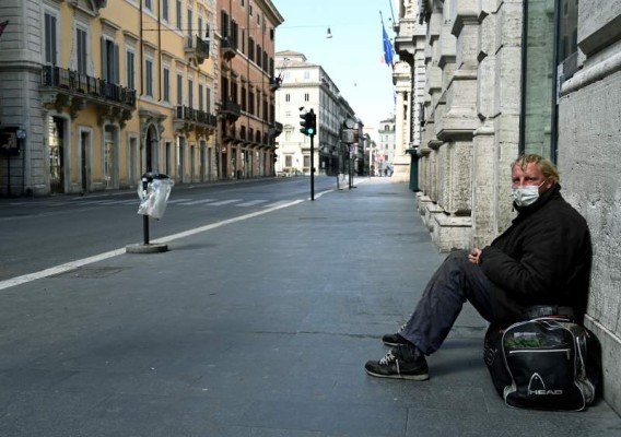 A homeless man sits in a deserted Via del Corso main street in central Rome on March 24, 2020 during the country's lockdown aimed at stopping the spread of the COVID-19 (new coronavirus) pandemic. (Photo by Vincenzo PINTO / AFP)