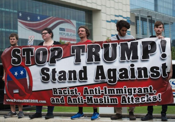 Protesters hold up a sign before the opening of the Republican National Convention on July 18, 2016 in Cleveland, Ohio.Thousands of delegates descend on a tightly secured Cleveland arena for the opening of the Republican National Convention, with Donald Trump's wife playing character witness as the tough-talking mogul seeks to lock up his party's presidential nomination. / AFP PHOTO / Andrew CABALLERO-REYNOLDS