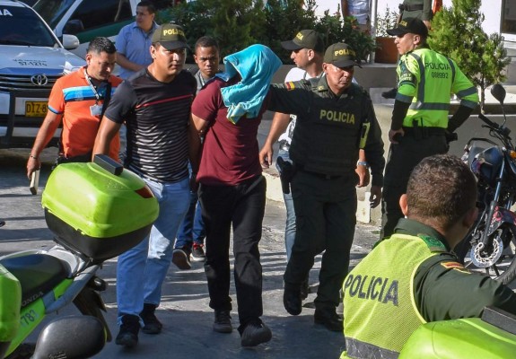 Police officers escort a bomb attack suspect in Barranquilla, Colombia, on January 27, 2018. At least three police officers were killed and fourteen other were wounded when alleged drug traffickers detonated a remote controlled bomb at a station in the northern city of Barranquilla, officials said. / AFP PHOTO