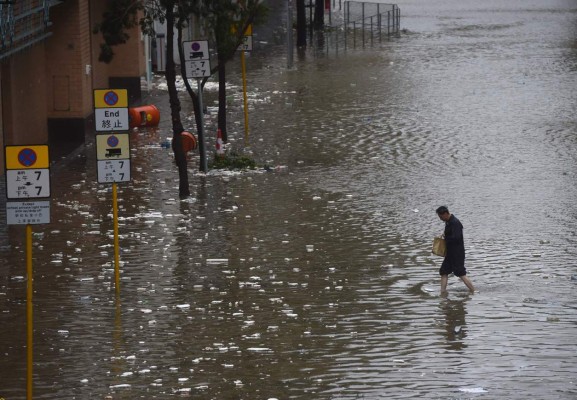 TOPSHOT - A man walks across a flooded street in the Heng Fa Chuen area as Typhoon Hato hits Hong Kong on August 23, 2017.Heavy rains and driving winds lashed Hong Kong on August 23 shutting schools and the stock market and bringing chaos to the city's international airport where hundreds of flights were cancelled. / AFP PHOTO / Anthony WALLACE
