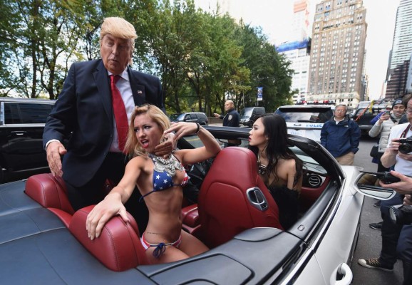 A Donald Trump impersonator with bikini clad models make their way to Trump Tower in a convertible October 25, 2016 in New York, as part of a performance art piece by British artist Alison Jackson. The event is to promote Jackson?s new show, ?Private,? in New York, which features staged photographs portraying the private lives of public individuals. / AFP PHOTO / TIMOTHY A. CLARY