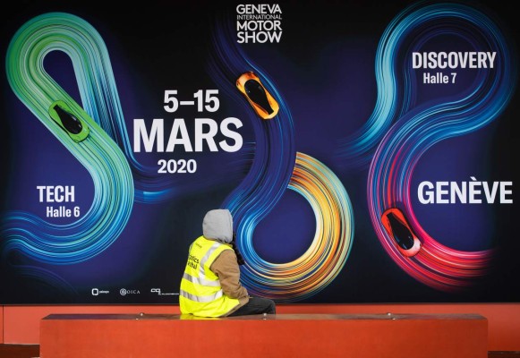 A worker sits next to a banner on February 28, 2020 at the Geneva International Motor Show which has been cancelled due to the novel coronavirus COVID-19 epidemic. - The Geneva International Motor Show, a major event on the auto industry calendar, has been cancelled after Switzerland banned large gatherings amid the new coronavirus epidemic, local authorities said Friday. (Photo by Richard Juilliart / AFP)