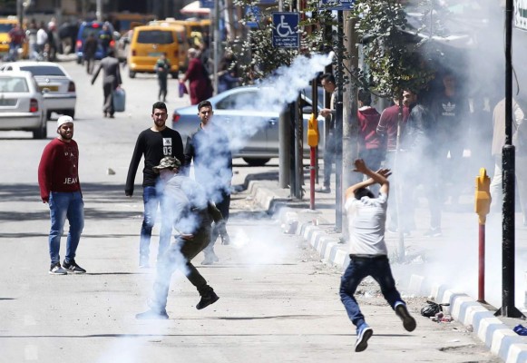 Palestinian demonstrators run for cover on March 31, 2018 during clashes with Israeli forces in occupied West Bank city of Hebron as a general strike is called for by local leaders in solidarity with Gaza. Sixteen Palestinians were killed and hundreds more wounded in the conflict's worst single day of violence since the 2014 Gaza war. Israel's military targeted three Hamas sites in the Gaza Strip with tank fire and an air strike after what it said was an attempted shooting attack against soldiers along the border that caused no injuries. Protesters, including women and children, gathered at multiple sites throughout the blockaded territory, which is flanked by Israel along its eastern and northern borders. / AFP PHOTO / HAZEM BADER