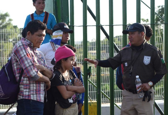 A Mexican migration officer speaks with Honduran migrants waiting to cross the international border bridge from Ciudad Tecun Uman in Guatemala to Ciudad Hidalgo in Mexico, on January 18, 2020. - On the eve, Mexican President Andres Manuel Lopez Obrador offered 4,000 jobs to members of the caravan in an attempt to dissuade them from traveling on to the United States. The caravan, which formed in Honduras this week, currently has around 3,000 migrants, Lopez Obrador said. (Photo by Johan ORDONEZ / AFP)