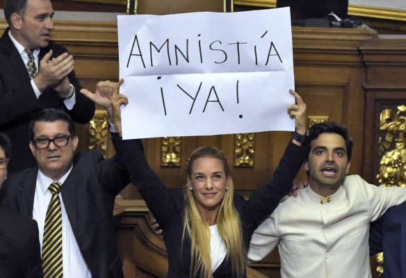 The wife of jailed Venezuelan opposition leader Leopoldo Lopez, Lilian Tintori (C) shows a banner asking for an immediate amnesty for political prisoners at the Venezuelan parliament in Caracas, on January 5, 2016. Venezuela's President Nicolas Maduro ordered the security forces to ensure the swearing-in of a new opposition-dominated legislature passes off peacefully Tuesday, after calls for rallies raised fears of unrest. AFP PHOTO/JUAN BARRETO