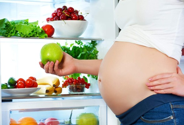 nutrition and diet during pregnancy. Pregnant woman standing near refrigerator with fruits and vegetables
