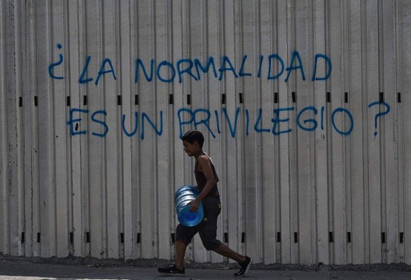 TOPSHOT - A boy carries a drum with water as he walks past a graffiti reading 'Is Normality a Privilege?' during a new power outage in Venezuela, at Fuerzas Armadas Avenue in Caracas on March 31, 2019. - Living conditions are plummeting in the oil-producing Latin American nation, which is spiralling ever deeper into economic chaos during a protracted political crisis. (Photo by Federico PARRA / AFP)