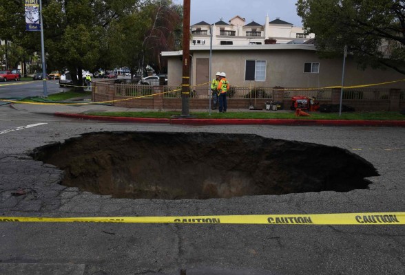 A large 20-foot-deep (6-meter) sinkhole that swallowed two vehicles in North Laurel Canyon Blvd, in Los Angeles, is cordoned-off on February 18, 2017, after a powerful storm hit southern California.The storm blew in from the Pacific Ocean, hitting California on February 17 with high winds, heavy rain that downed power lines, leaving 60,000 people in the Los Angeles area without power, and prompting hundreds of flight delays and cancellations at airports. Four people have been reported killed due to the storm. / AFP PHOTO / Mark RALSTON