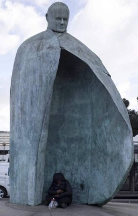 Un indigente se refugia bajo la estatua del papa Juan Pablo II, en Roma.