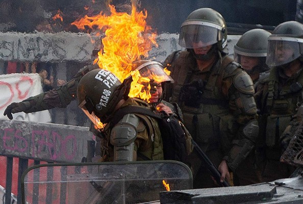 TOPSHOT - A riot police officers is reached by a petrol bomb during clashes with demonstrators protesting against the economic policies of the government of President Sebastian Pinera, in Santiago, on November 4, 2019. - Unrest began in Chile last October 18 with protests against a rise in transport tickets and other austerity measures and descended into vandalism, looting, and clashes between demonstrators and police. Protesters are angry about low salaries and pensions, poor public healthcare and education, and a yawning gap between rich and poor. (Photo by CLAUDIO REYES / AFP)