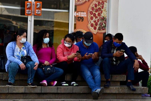 People sit wearing face masks outside a restaurant in Tegucigalpa, on April 3, 2020 during the novel coronavirus (COVID-19) outbreak. - Latin America is heading into 'a deep recession' in 2020, with an expected drop in the region's GDP of 1.8 to 4.0 percent due to the coronavirus pandemic, the UN economic commission for the region said Friday. (Photo by ORLANDO SIERRA / AFP)