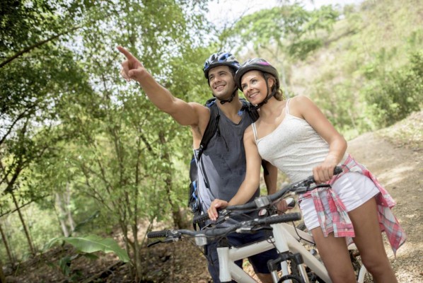 Young Latin American couple mountain biking and pointing the road ahead