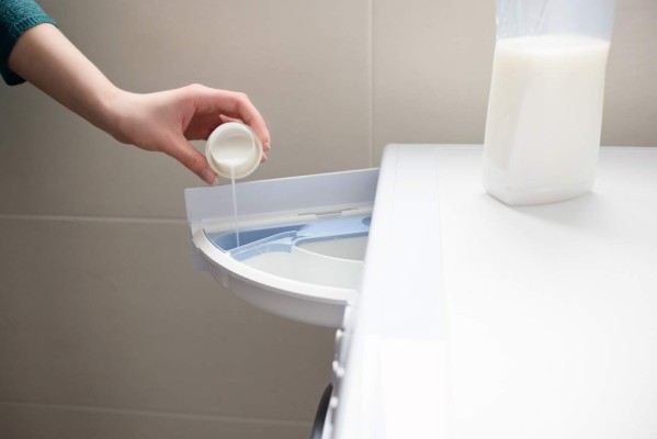 Closeup of a woman's hand pouring liquid fabric softener to the washing machine