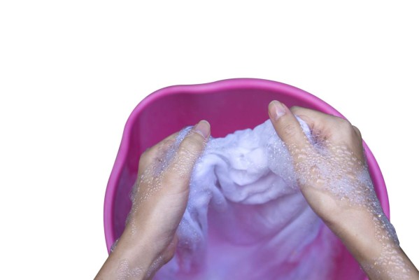 Female Hand washing clothes in the pink basin.