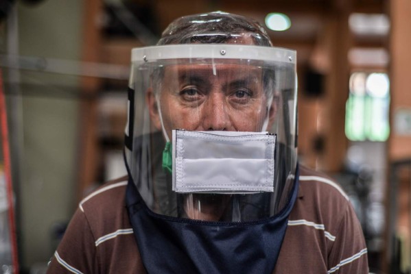 A man wears a face shield against the spread of the new coronavirus as the ones that are manufactured at the workshop where he works in Soacha, metropolitan area of Bogota, Colombia, on April 30, 2020. (Photo by Diana Sanchez / AFP)