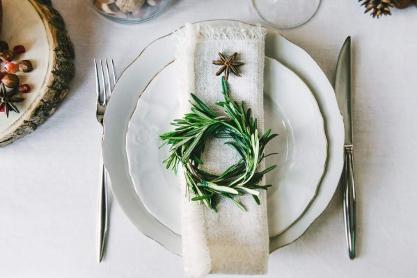 Decorative green wreath on a napkin as a part of table appointments, clean white tablecloth background, top view. Christmas table place setting.