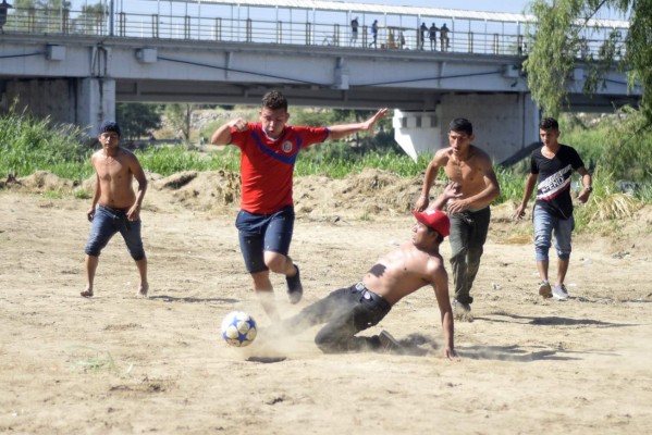 Central American migrants -mostly Hondurans heading in a caravan for the US- play football on the bank of the Suchiate river, in Tecun Uman, Guatemala, on the border with Ciudad Hidalgo, Mexico, on January 21, 2020. - Some 500 Central Americans, from the so-called '2020 Caravan', crossed Monday from Guatemala to Mexico, but over 400 were intercepted when National Guardsmen fired tear gas at them. (Photo by Johan ORDONEZ / AFP)