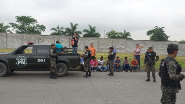 Tres agentes de la Policía Militar de Honduras, custodian a dos detenidos e investigan a 15 retenidos en la Gran Terminal Metropolitana de Buses de San Pedro Sula.