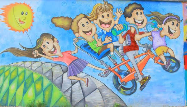 Una pintura muestra a varios niños y niñas divertirse, junto al sol, en una bicicleta de ensueño.