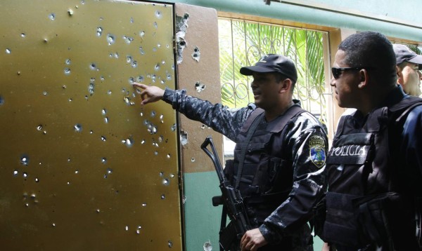 El jefe de la DNIC, Manuel Calderón, a la derecha, y un efectivo del escuadrón Cobra, observan el portón de la casa donde se dio el enfrentamiento, el cual tiene 140 perforaciones de bala.