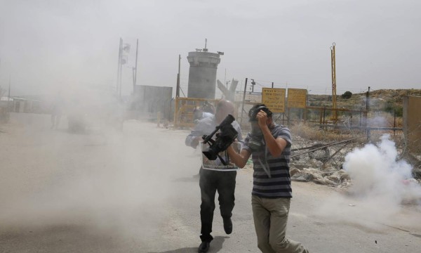 Palestinian journalists run for cover from tear gas canisters fired by Israeli forces during a demonstration in support of Palestinian journalists on the occasion of the World Press Freedom day outside the compound of the Israeli-run Ofer prison near Betunia in the occupied West Bank, on May 3, 2016 / AFP PHOTO / ABBAS MOMANI