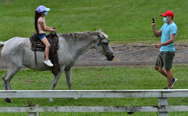 A man takes a picture of a girl on a horse on the shore of Lake Yojoa, largest natural lake in Honduras, in Santa Cruz de Yojoa municipality, some 180 km northwest of Tegucigalpa, on September 6, 2020, amid the COVID-19 novel coronavirus pandemic. - The novel coronavirus has killed 2,000 people in Honduras in the first six months since the pandemic erupted in the country, with more than 64,500 contagions. As the country is gradually reopening the economy, thousands of Hondurans have turned to the mountains and other tourist places that give them security. One of the most visited places is Lake Yojoa. (Photo by Orlando SIERRA / AFP)