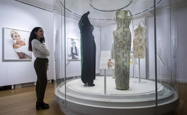 Una empleada posa hoy junto a varias fotografías y algunos de los vestidos de la princesa Diana de Gales, durante el pase para la prensa de la exposición 'Diana: Her Fashion Story', en el palacio de Kensington en Londres, Reino Unido. EFE